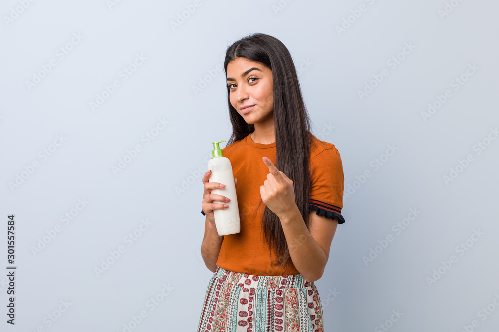 Young arab woman holding a cream bottle pointing with finger at you as if inviting come closer. Young arab woman holding a cream bottle pointing with finger at you as if inviting come closer.