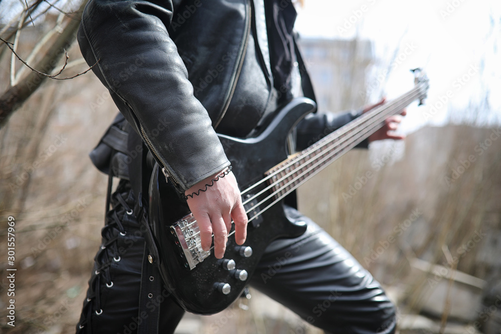 Rock guitarist on the steps. A musician with a bass guitar in a leather suit. Metalist with a guitar on the background of industrial steps.