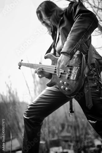 Rock guitarist outdoor. A musician with a bass guitar in a leather suit. Metalist with a guitar on the background of industrial steps.