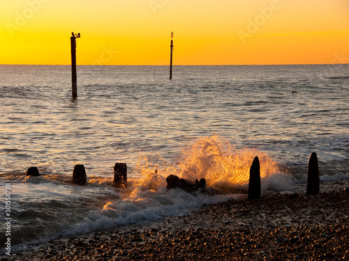 Waves break over a groyne at sunset onto Southwick Beach in West Sussex