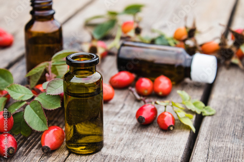 Glass bottle of rosehip essential oil with fresh rosehips on a wooden table. Tincture or essential oil with rose hips.