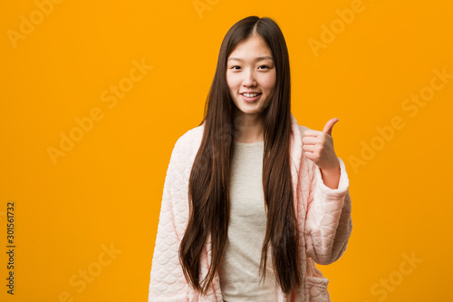 Young chinese woman in pajama smiling and raising thumb up