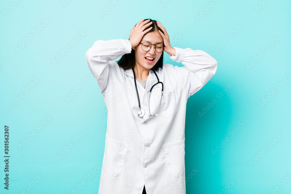 Young chinese doctor woman laughs joyfully keeping hands on head. Happiness concept. Young chinese doctor woman laughs joyfully keeping hands on head. Happiness concept.