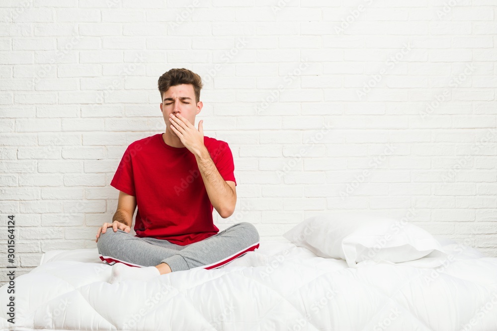 Young teenager student man on the bed yawning showing a tired gesture covering mouth with hand. Young teenager student man on the bed yawning showing a tired gesture covering mouth with hand.