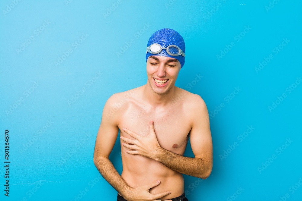 Young swimmer man laughs happily and has fun keeping hands on stomach.