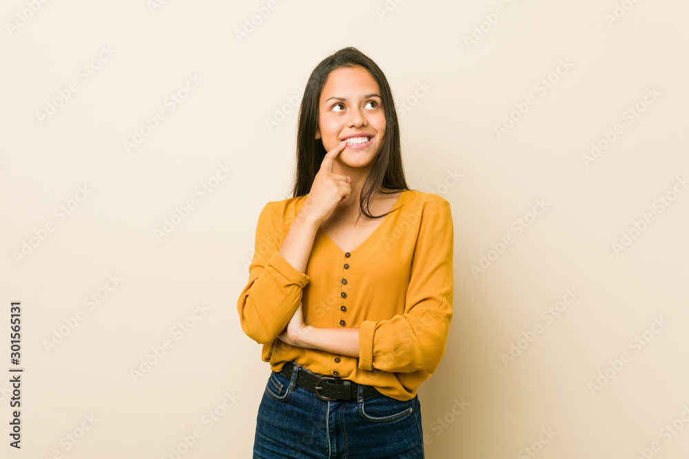 Young hispanic woman against a beige background relaxed thinking about something looking at a copy space. Young hispanic woman against a beige background relaxed thinking about something looking at a copy space.