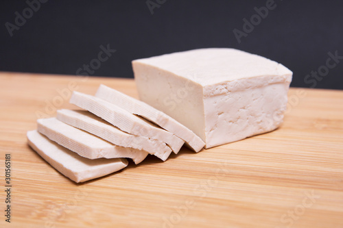 Tofu firme troceado sobre una tabla de madera en un fondo negro.