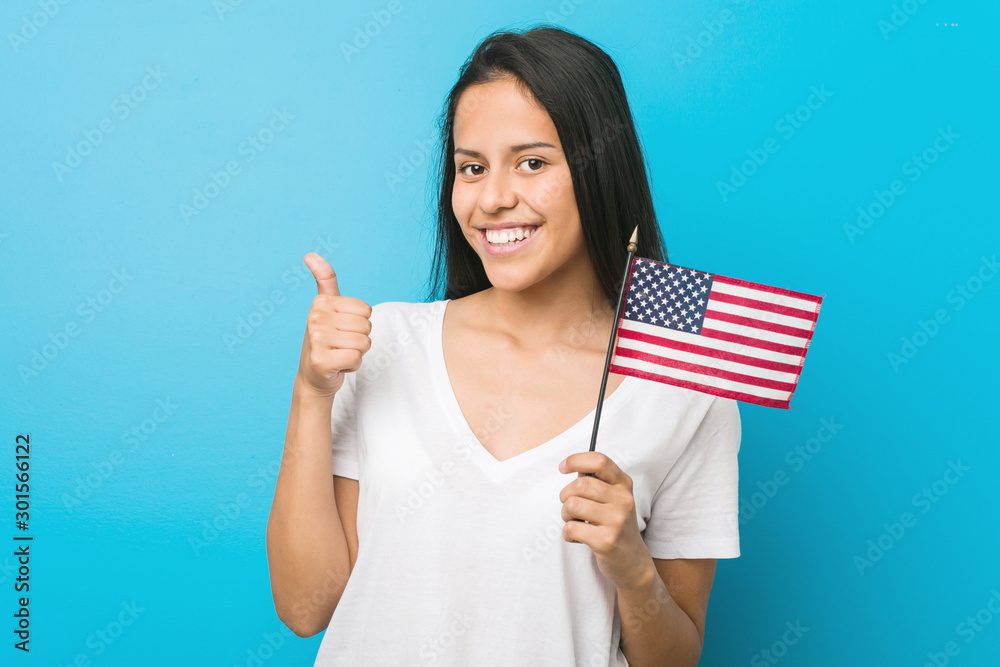 Young hispanic woman holding a united states flag smiling and raising thumb up Young hispanic woman holding a united states flag smiling and raising thumb up