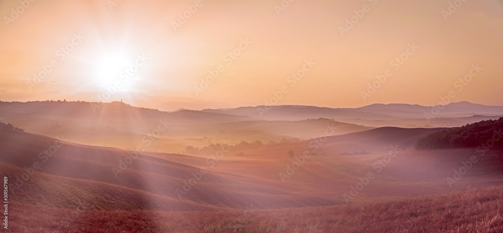 Beautiful panorama of pink landscape with rolling hills, crepuscular sun rays at summer sunrise near Pienza. Travel destination Tuscany, Italy. Copy space