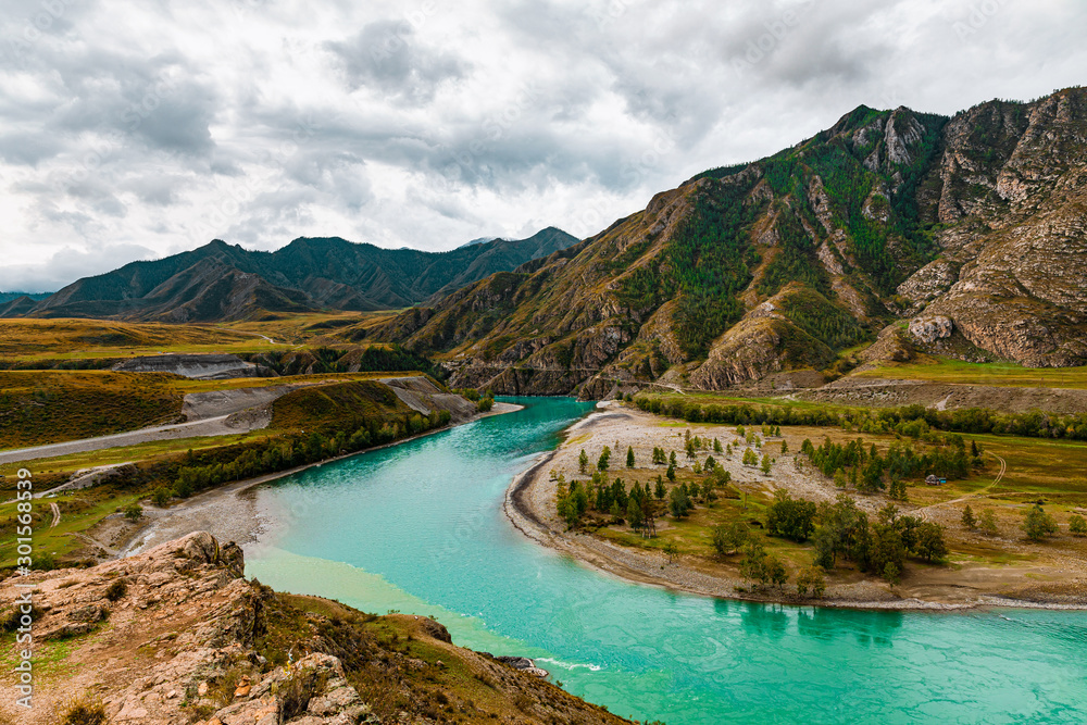 Panorama of mountain river on background of beautiful mountains in cloudy weather. View of turquoise river in the mountains on the background gloomy sky