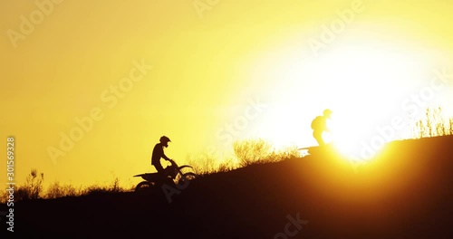 Extreme sport adventure of motorbikers in mountains with beautiful orange sundown. Silhouette of two motorcyclists riding off road on mountains at sunset, side view. Freeride driving on motorbikes. photo