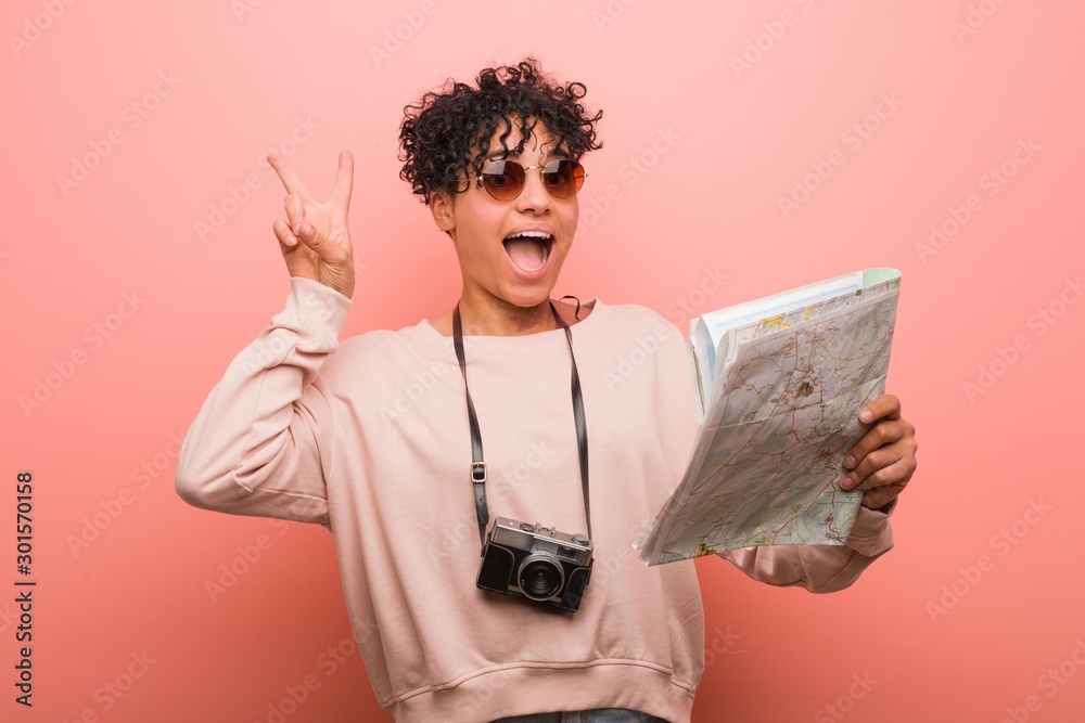 Foto Young african american woman holding a map showing victory sign and smiling broadly