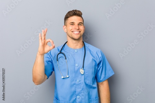 Young nurse man cheerful and confident showing ok gesture. photo