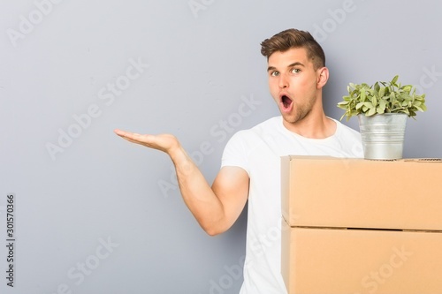 Young man doing a move holding boxes impressed holding copy space on palm.