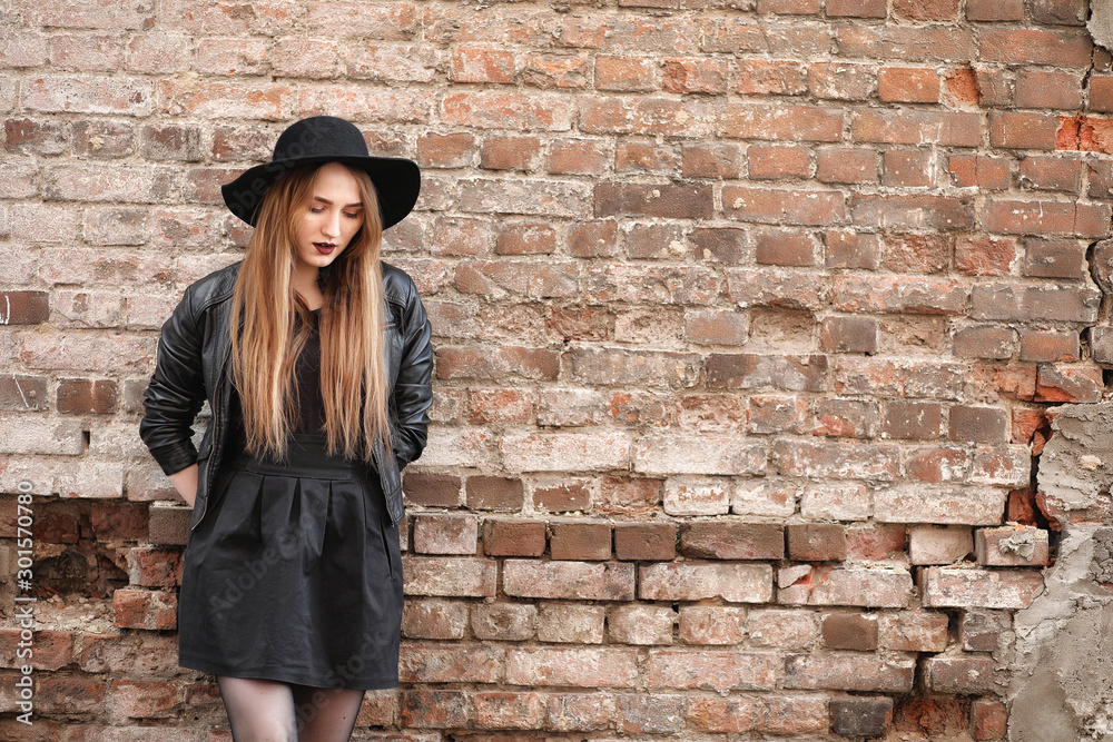 Young beautiful girl in a hat and with a dark make-up outside. Girl in the Gothic style on the street. A girl walks down the city street in a leather waistcoat with a phone.