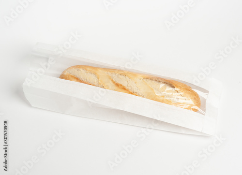 Loaf of fresh baked artisan baguette bread in market paper bag over white background. Top view, copy space. Packaging concept