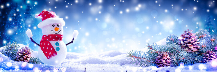 Happy Snowman On Snowy Wooden Table Decorated With Pine-cones And Branches - Christmas / Winter