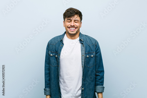 Young hispanic cool man laughs and closes eyes, feels relaxed and happy.