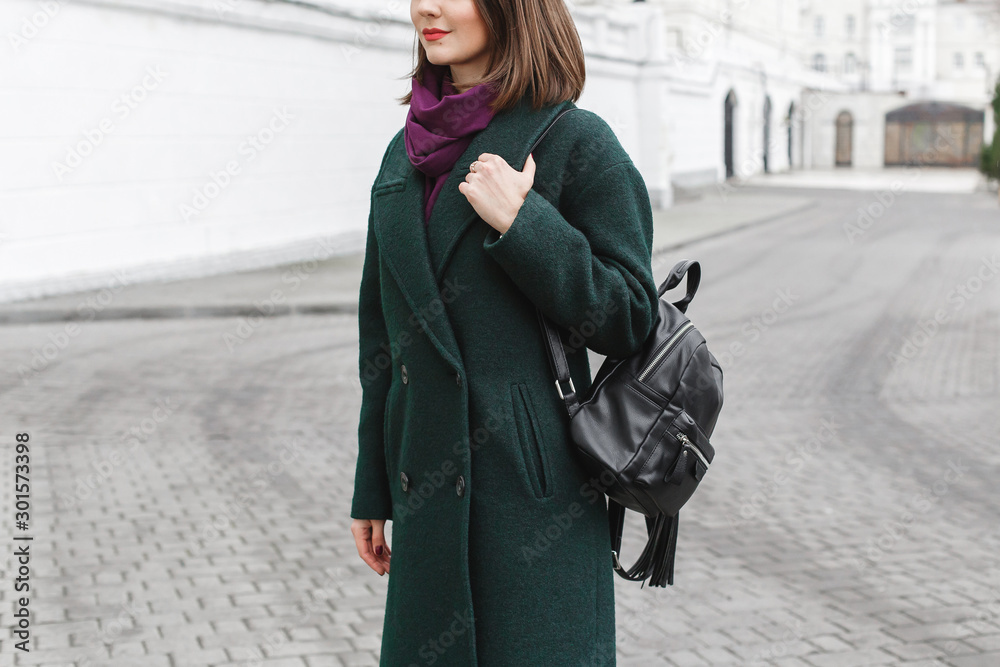 Backpack in woman's hands. Young woman in green coat holding black backpack.  Trendy stylish casual outfit. Details of everyday autumn, winter or spring  look. Street fashion. Stock Photo | Adobe Stock