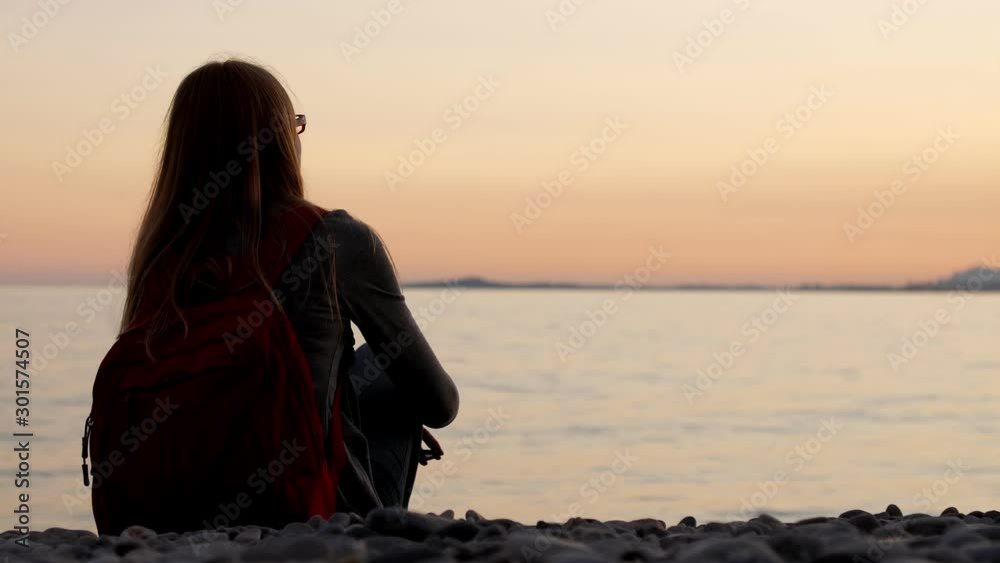 Silhouette of a Girl Sitting on the Beach at Sunset. Romantic scene lonely woman on the beach in the evening. Calm sea waves.