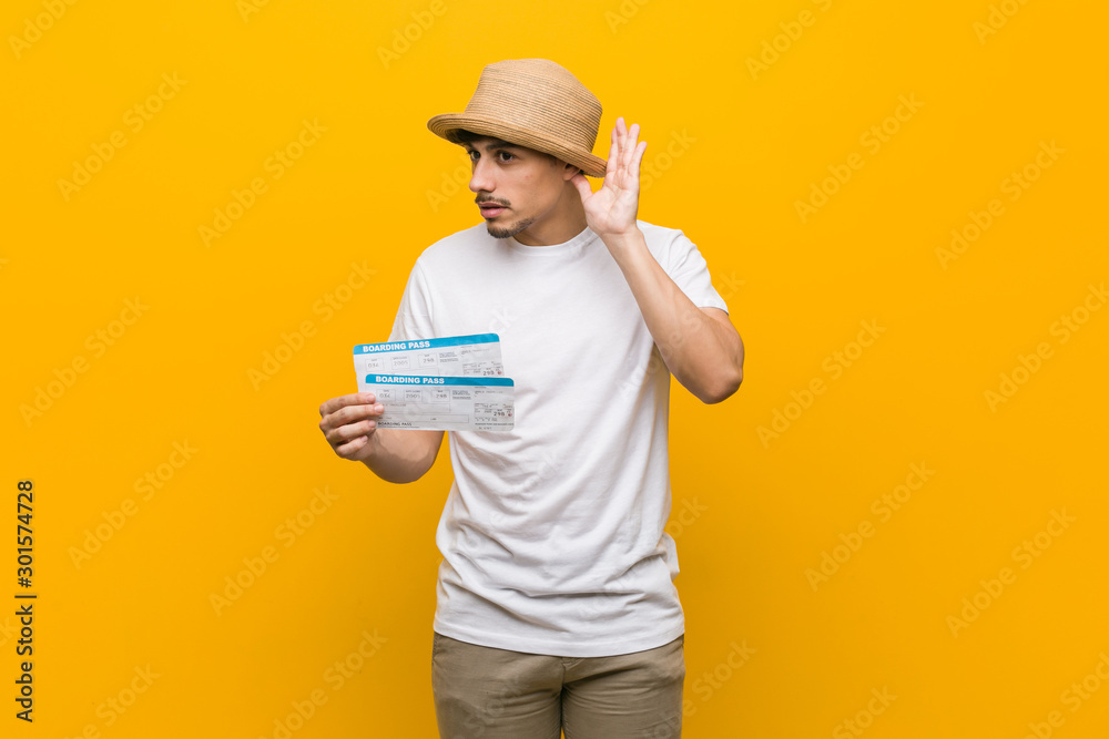 Young hispanic man holding an air tickets trying to listening a gossip.