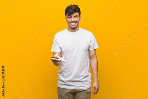 Young hispanic man holding an airplane icon happy, smiling and cheerful.