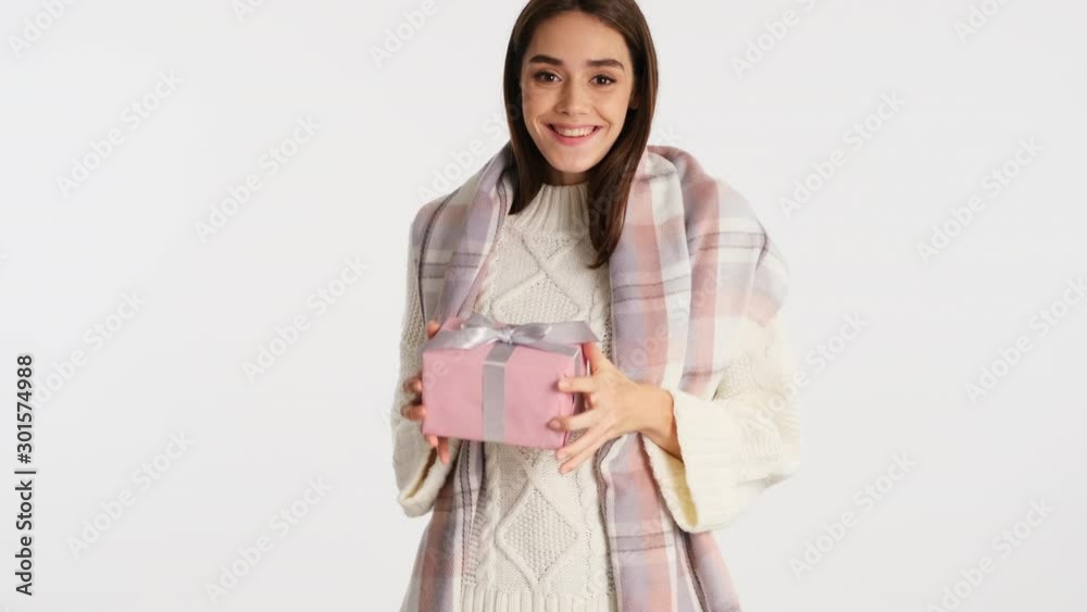 Attractive cheerful girl with cozy plaid on shoulders happily throws up gift box over white background Attractive cheerful girl with cozy plaid on shoulders happily throws up gift box over white background