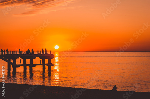 Colorful sunset at the sea and a pier with fishermen.