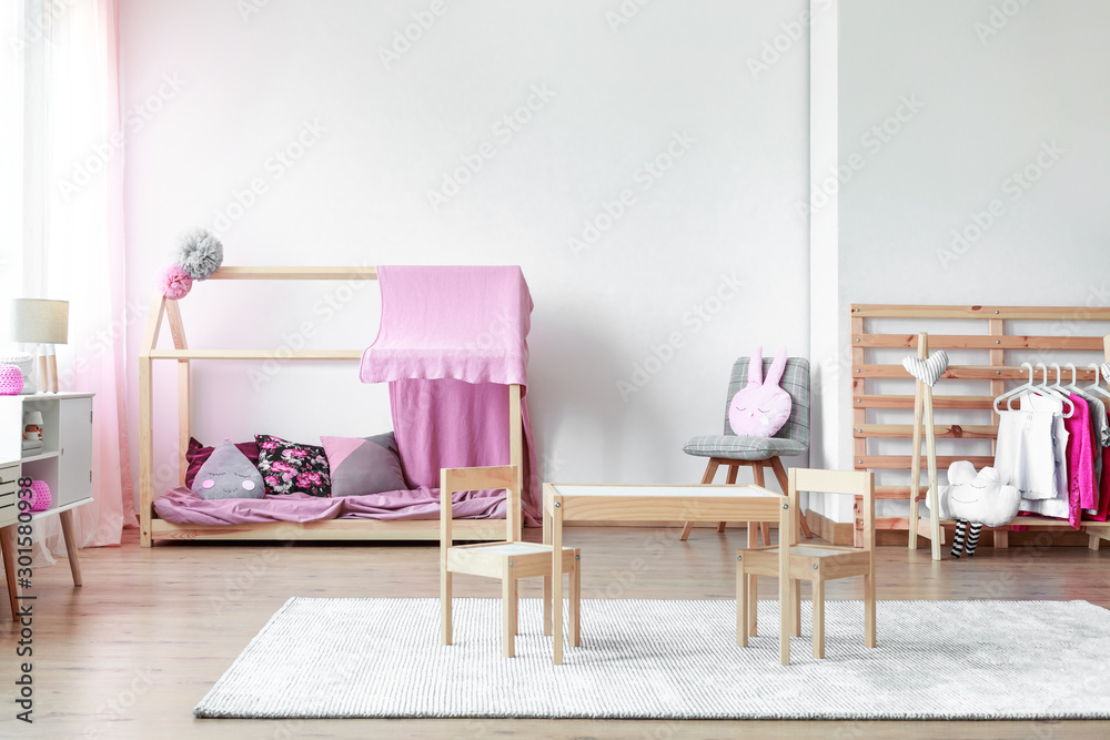 Fototapeta premium Copy space on empty white wall in stylish pink and bright baby room with wooden furniture
