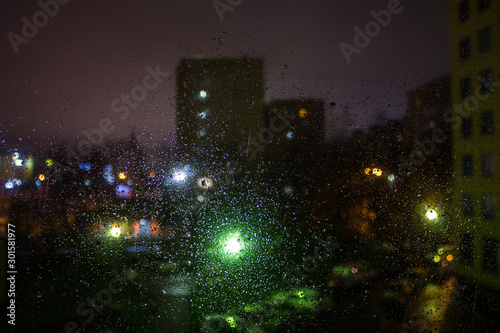Night city view through wet glass soft focus
