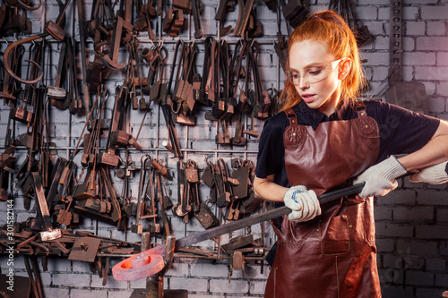 redhead ginger woman working smithytools in dark workplace forging hammering malleation details. small business concept photo