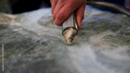 close shot of tourist activity at the Boyne valley tombs. handheld shot of a hand holding a steel mantled carving stone and carving an artisan pattern in limestone. Lower frame copy space. photo