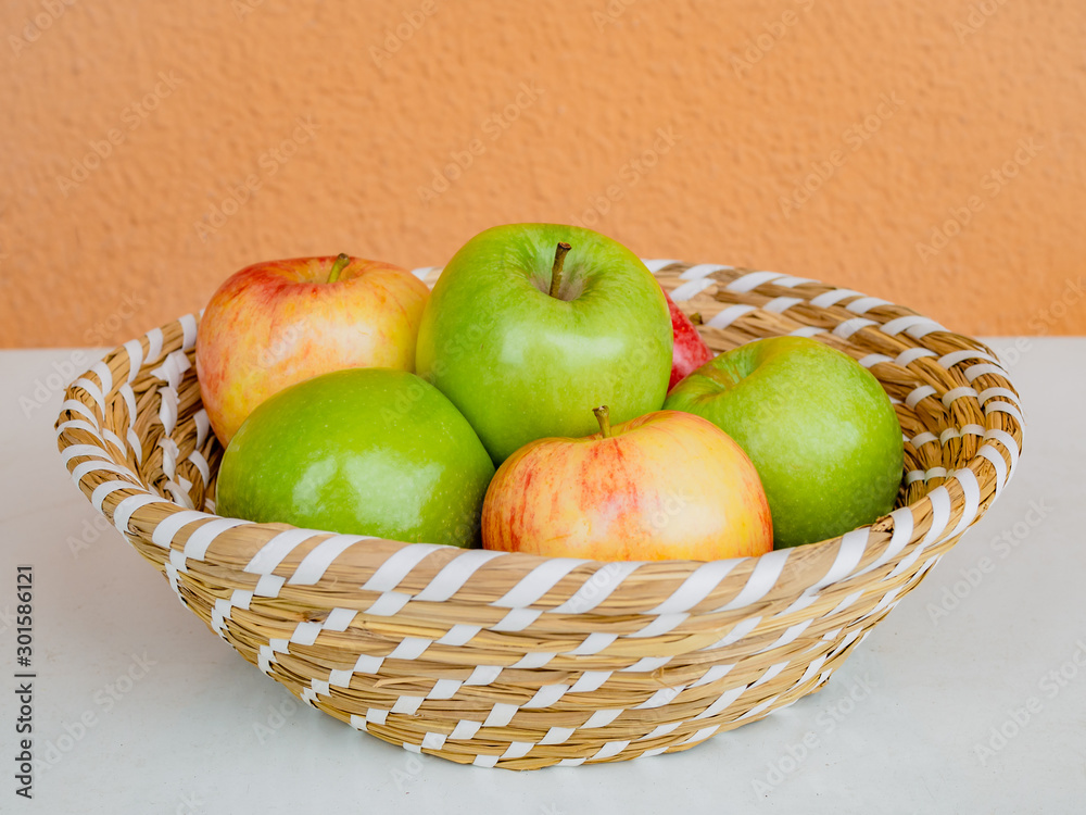 Red and green apples in the basket, at the white table Red and green apples in the basket, at the white table