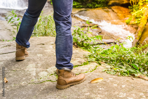 Legs of man wear jeans standing on big stone near waterfall for adventure