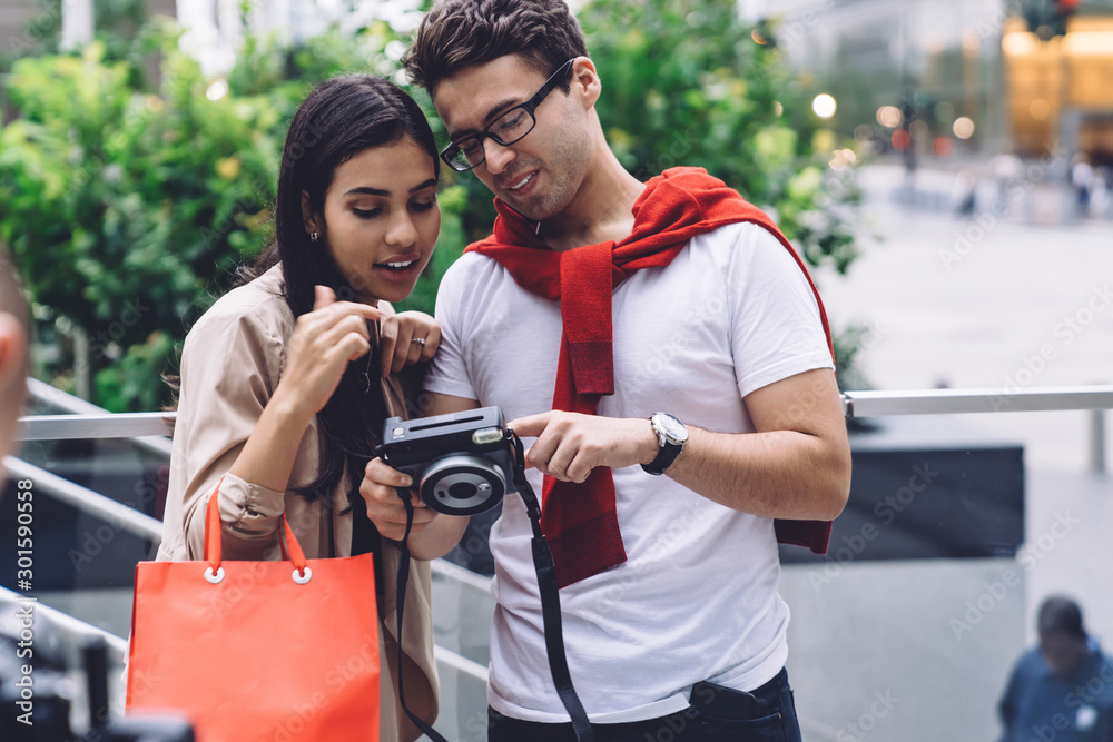 Stylish joyful multiethnic couple using photo camera on street