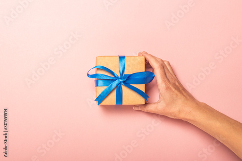 Female hand takes a gift on a pink background with confetti. Gift concept for a loved one, holiday, christmas. Flat lay, top view