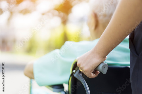 Happy Family or caregivers with elderly in a wheelchair while spending time together. close up of hand Assistant or carer supporting patient disabled in wheelchair relaxing and walking outside at park