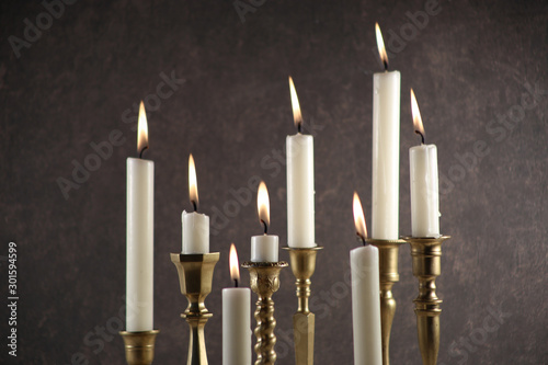 Burning candles in vintage metal candlesticks against dark stone background..