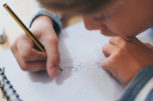 Close up view of student drawing with pencil. Boy doing homework writing on a paper. Kid hold a pencil and draw a manga at home. Teen drawing sitting at the table. Education art talent ability concept photo