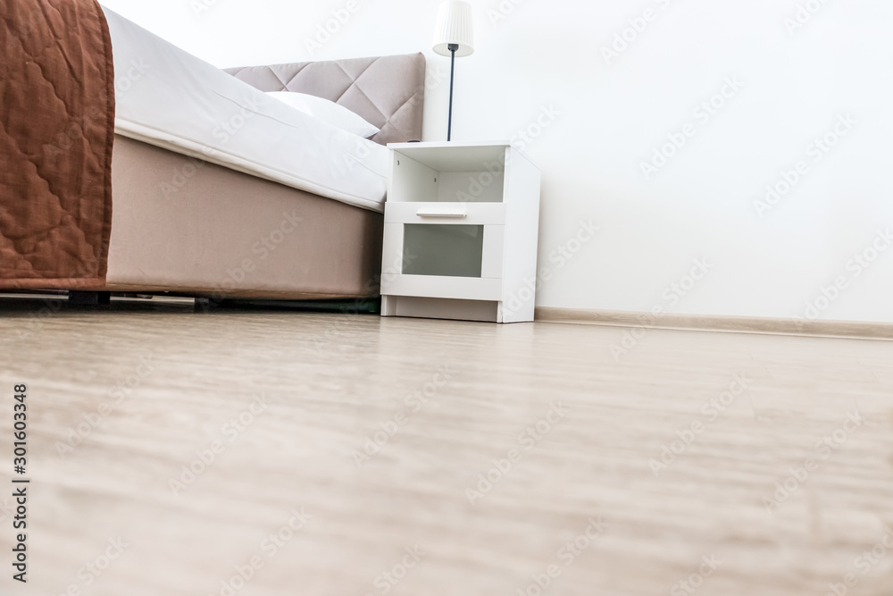 Empty white bedroom interior with copy space on the floor, low angle shot of a bed and a nightstand Empty white bedroom interior with copy space on the floor, low angle shot of a bed and a nightstand