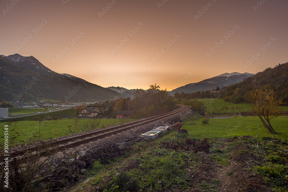 Countryside landscape with mountains in the background at sunset. Yellow and red sky with clouds
