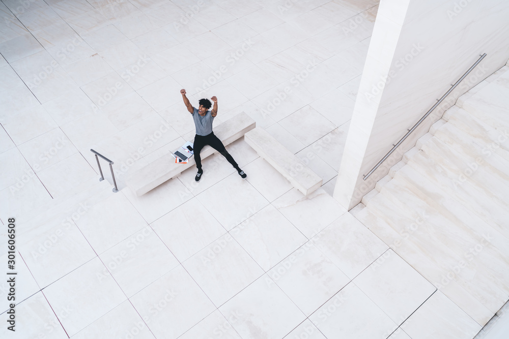 © BullRun - Happy man in casual wear overjoyed with finish of startup project developing with modern laptop computer, accomplished Latino male freelancer with raised hands celebrating approved remote work