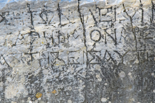 Half-erased ancient Greek letters embossed on an old gray marble slab covered with cracks and mold.