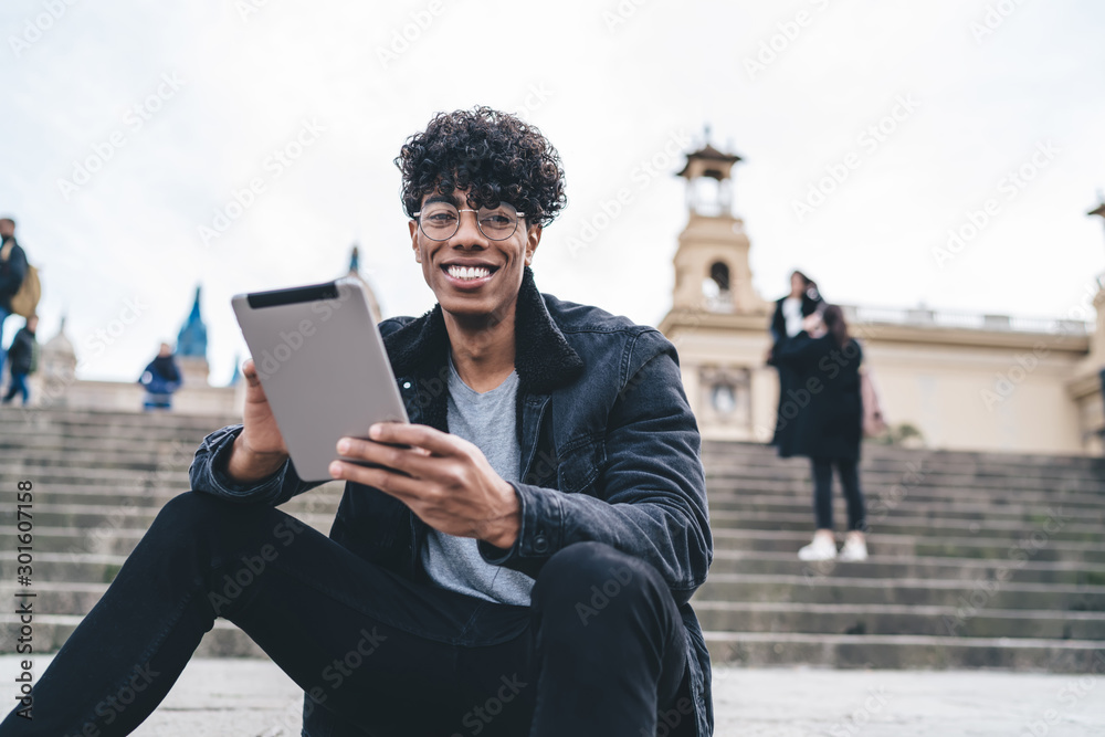 Black student with tablet sitting on city stairs