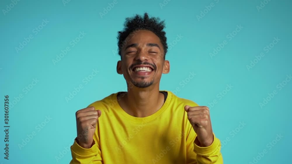 Man shows yeah gesture of victory,he achieved result, goals. Surprised excited happy african guy on blue background Man shows yeah gesture of victory,he achieved result, goals. Surprised excited happy african guy on blue background