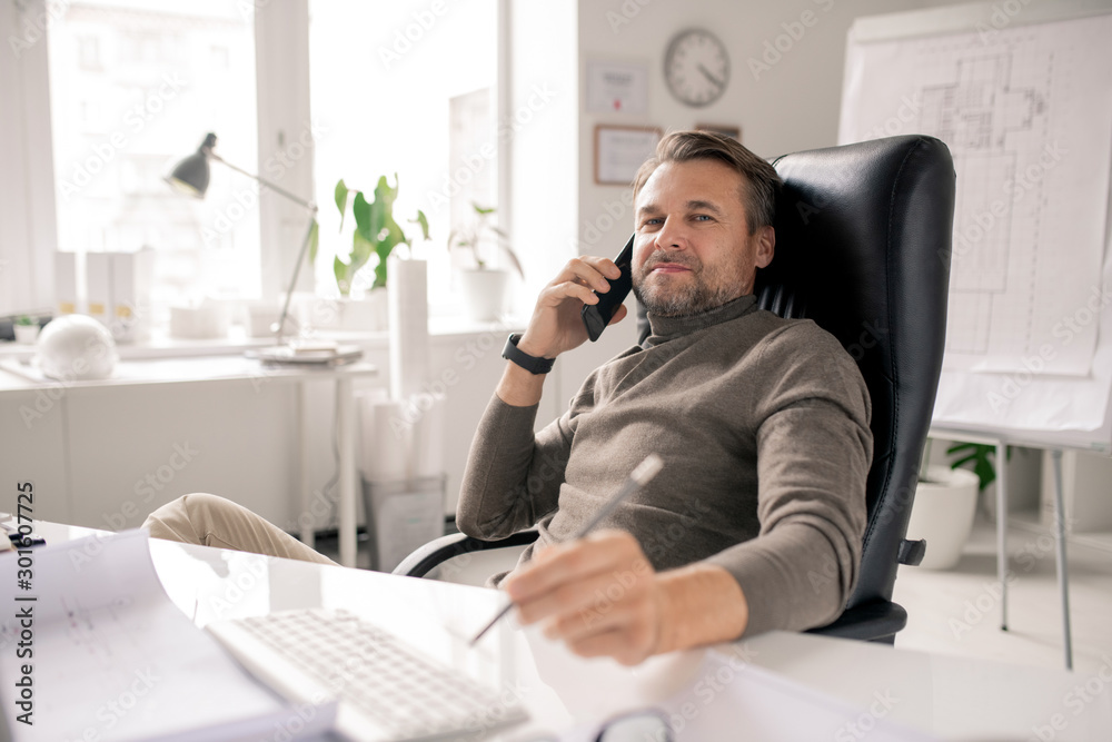 Fototapeta premium Serious mature businessman or agent consulting clients by desk in office