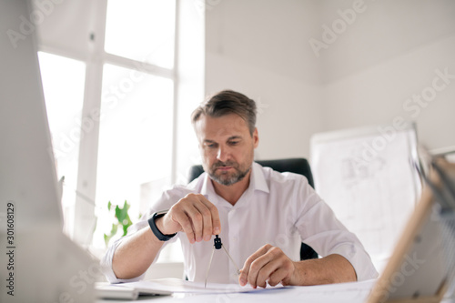 Mature bearded engineer in white shirt using dividers while working over sketch