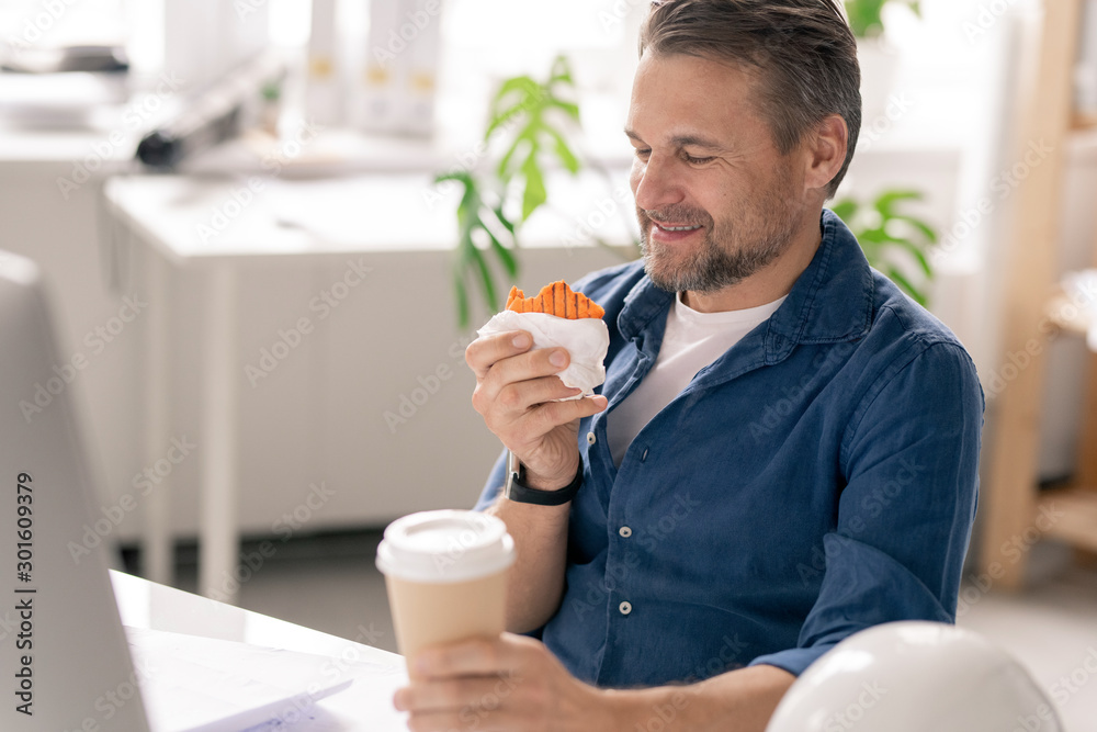 Cheerful engineer with drink and dessert looking at cupcake with funny fish Cheerful engineer with drink and dessert looking at cupcake with funny fish