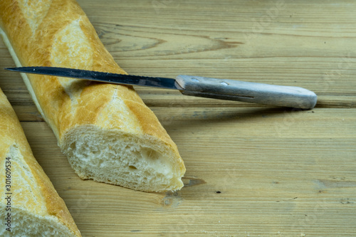French baguette cut in half. Freshly baked traditional french bread on a wooden table next to a kitchen knife.