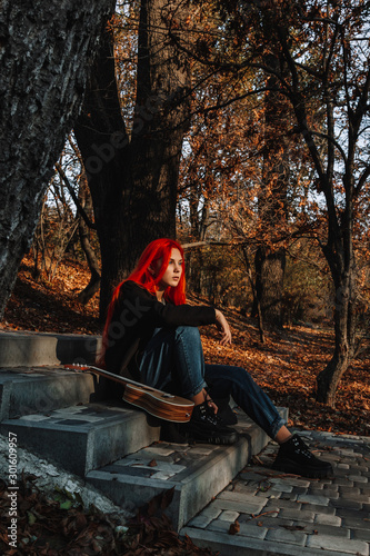 Sexy beautiful redhead girl with magnificent long hair. Ukulele playing, sitting on the steps in the park. Perfect woman portrait. Musical education, street performer.